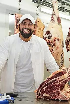 Inhaber Yusuf Turna mit Biofleisch auf dem Metzgertisch. Im hintergrund abgehangenes Biorindfleisch